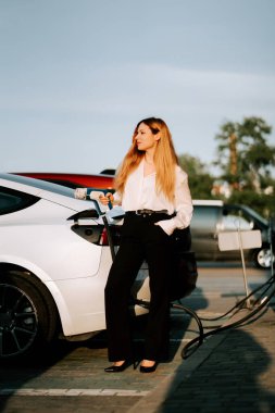 Kızıl saçlı genç bir kadın güneşli bir öğleden sonra alışveriş merkezinde elektrikli araç yüklüyor.