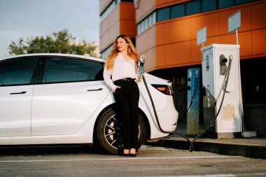 Kızıl saçlı genç bir kadın alışveriş merkezinde güpegündüz elektrikli araba şarj ediyor.