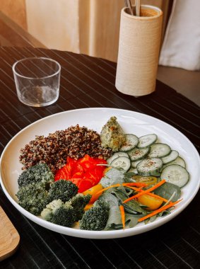 Modern yemek masasında servis edilen taze sebzeli renkli kinoa salatası.