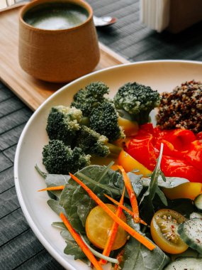 Renkli vejetaryen salatası, kinoalı ve ahşap bir masada yeşil çay.