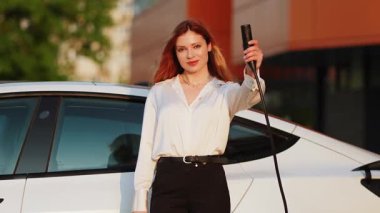 Genç kadın, şehir merkezindeki şarj istasyonunda gündüz vakti elektrikli araba şarj ediyor.