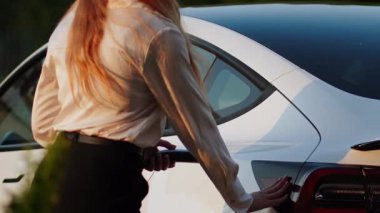 Genç bir kadın yeşil bir ortamda akşam saatlerinde istasyonda elektrikli araba yüklüyor.