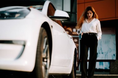 Sakin bir şehir ortamında gün batımında kadın otoparkta elektrikli araba yüklüyor.
