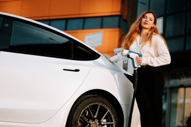 Güneşli otoparkta gün batımında kadın elektrikli araba şarj ediyor.