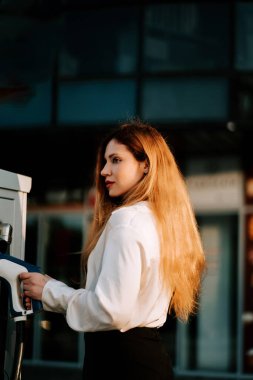 Kadın gün batımında otoparkta elektrikli arabayı şarj ediyor.