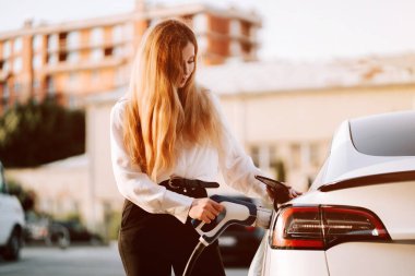 Güzel günbatımında kadın otoparkta elektrikli araç yüklüyor.
