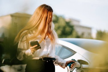 Şehir merkezinin yakınındaki güzel günbatımında kadın otoparkta elektrikli araba yüklüyor.
