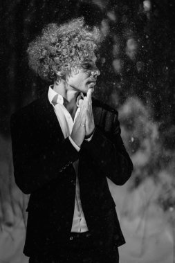 Bir kar yağışı sırasında siyah bir takım elbiseyle manken, düşünceli bir şekilde dışarıda poz verir.