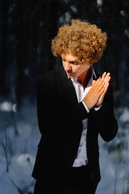 Gündüz vakti resmi giyinmiş genç adam karlı ormanda poz veriyor.