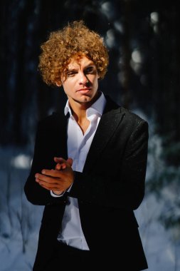 Siyah takım elbiseli genç adam kış öğleden sonra karlı ormanda kutlama yapar.