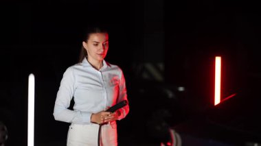 Kadın gece vakti yeraltı otoparkında elektrikli araba şarj ediyor.