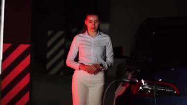 Kadın akşam saatlerinde yeraltı otoparkında elektrikli araba şarj ediyor.