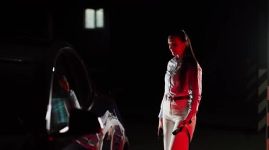 Kadın akşam saatlerinde yeraltı otoparkında elektrikli araba şarj ediyor.