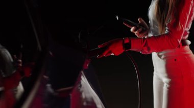 Kadın gece vakti otoparkta elektrikli arabayı şarj ediyor.