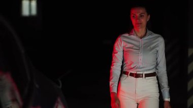 Kadın, akşam saatlerinde otoparkta elektrikli araba şarj ediyor.