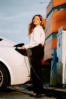 Kızıl saçlı genç bir kadın gün batımında şehrin yakınlarında elektrikli araba kullanıyor.