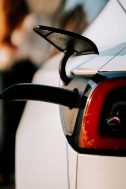 Kızıl saçlı genç bir kadın gün batımında bir istasyonda elektrikli araba şarj ediyor.