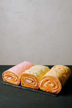 Renkli yuvarlanmış tatlılar bej arkaplanlı bir tahta tepside dizilmiş.