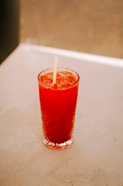 Açık renkli bir yüzeyde, uzun bir bardakta servis edilen kırmızı içeceği tazeliyorum.