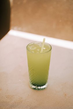 Güneşli bir öğleden sonra açık bir kafede uzun bir bardakta servis edilen ferahlatıcı yeşil içecek.