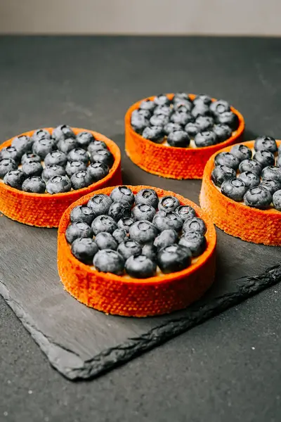 Taze pişmiş yaban mersinli turtalar mutfak ortamında siyah bir tahtada sergileniyor.