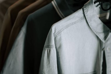 Öğleden sonra ışığı altında minimalist bir ortamda askılarda sergilenen yumuşak kumaş gömlekler