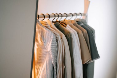 İyi aydınlatılmış bir odada askıda asılı duran düzgünce düzenlenmiş gömlek koleksiyonu.