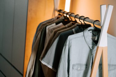 Gündüz saatlerinde modern bir iç mekan ortamında giysiler askıda asılı.