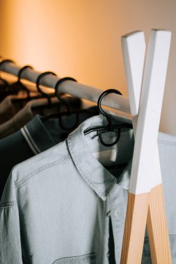 Modern iç mekanda yumuşak ışıklandırmalı ahşap rafta şık kıyafetler sergileniyor.