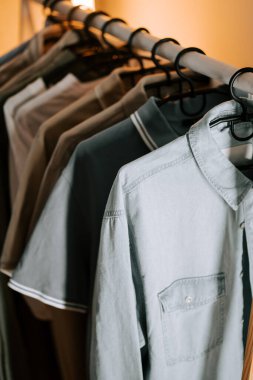 Ilık aydınlatma ortamında askıda asılı duran sıradan gömleklerin moda gösterisi.