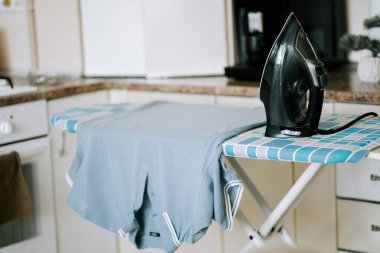 Demir, yakındaki mavi yakalı gömlekli desenli ütü masasına dayanır.