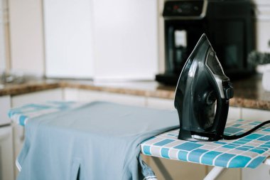 Siyah ütü mutfaktaki mavi kareli ütü masasında duruyor.