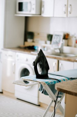 Ütü masasındaki siyah ütü gün boyu açık bir mutfakta.