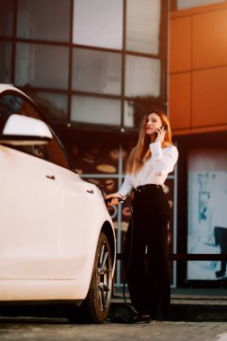 Kızıl saçlı bir iş kadını şehir merkezindeki bir şarj istasyonunda elektrikli arabasını şarj ediyor.