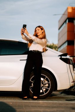 Kızıl saçlı bir iş kadını güneşli bir günde istasyonda elektrikli araba yüklüyor.