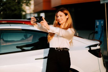 Kızıl saçlı bir iş kadını güpegündüz istasyonda elektrikli arabayı şarj ediyor.