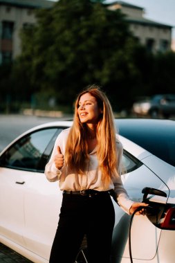 Kızıl saçlı bir iş kadını, şehir merkezindeki şarj istasyonunda elektrikli araba kullanıyor.