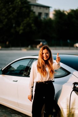 Şehirdeki şarj istasyonunda kızıl saçlı bir iş kadını elektrikli araba kullanıyor.