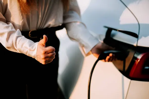 Kızıl saçlı bir iş kadını gün batımında bir istasyonda elektrikli araba alıyor.