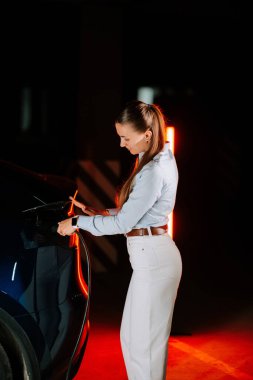Kadın gece vakti yeraltı otoparkında elektrikli araba şarj ediyor.