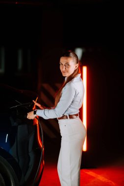 Kadın akşam saatlerinde yeraltı otoparkında elektrikli araç yüklüyor.