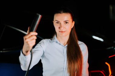 Kadın akşam saatlerinde yeraltı otoparkında elektrikli araba şarj ediyor.