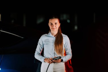 Kadın gece vakti yeraltı otoparkında elektrikli araba şarj ediyor.
