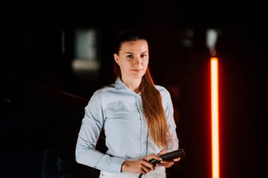 Kadın akşam saatlerinde yeraltı otoparkında elektrikli araba şarj ediyor.