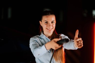 Kadın, yeraltı otoparkında gülümseyen ve baş parmağını kaldıran elektrikli arabayı şarj ediyor.