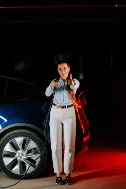 Yeraltı otoparkında kadın elektrikli araba yüklüyor. Pozitif tutum ve modern kıyafetlerle.