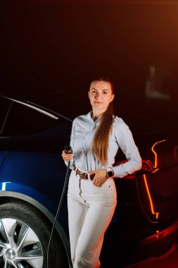 Kadın akşam saatlerinde yeraltı otoparkında elektrikli araca yükleniyor.
