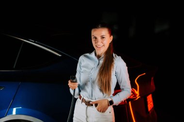 Kadın akşam saatlerinde yeraltı otoparkında elektrikli araba şarj ediyor.