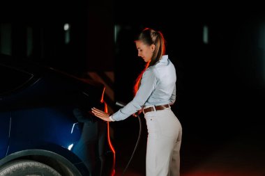 Kadın akşam saatlerinde yeraltı otoparkında elektrikli araç yüklüyor.