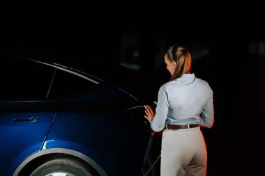 Gece yarısı yeraltı otoparkında elektrikli araba şarj eden bir kadın.